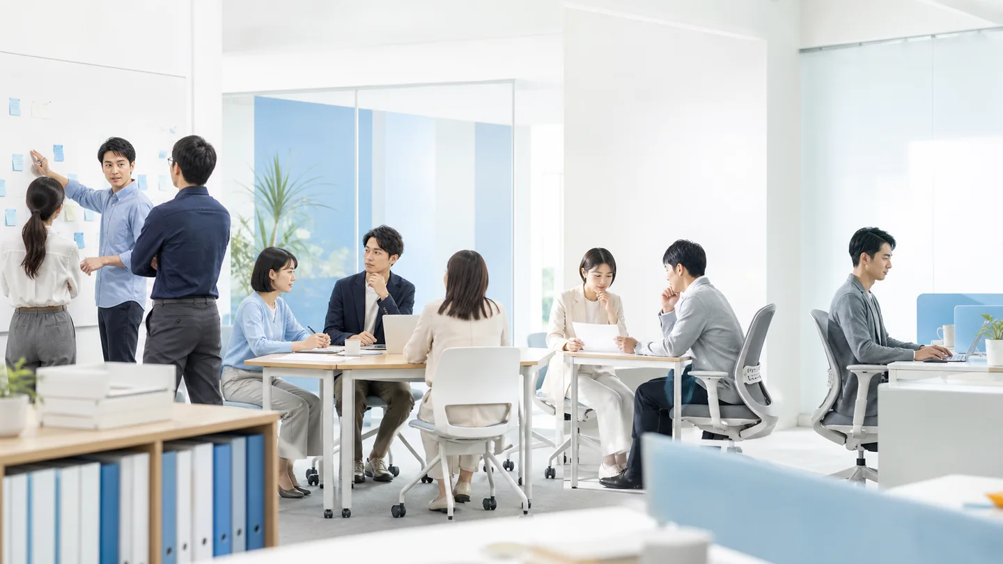 明るいオフィスで、複数のチームがAI活用の方針や業務への適用を話し合う様子